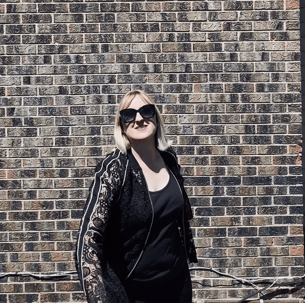 Christine DeHerrera wearing a black lace jacket spinning in front of a red brick wall
